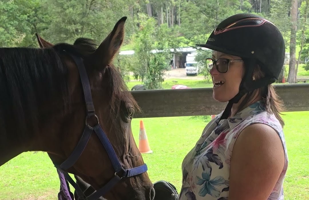 A smiling participant in a riding helmet face to face with a horse
