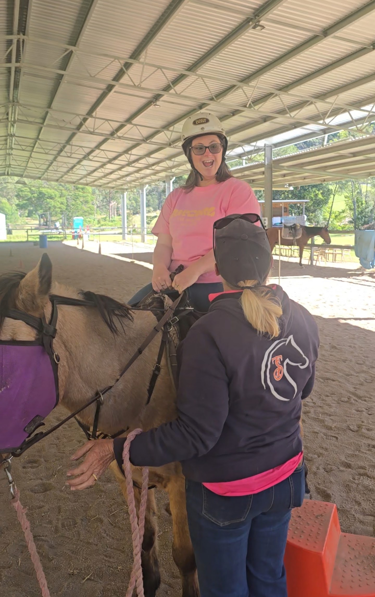 A beaming participant in a helmet sitting on horseback at a riding arena